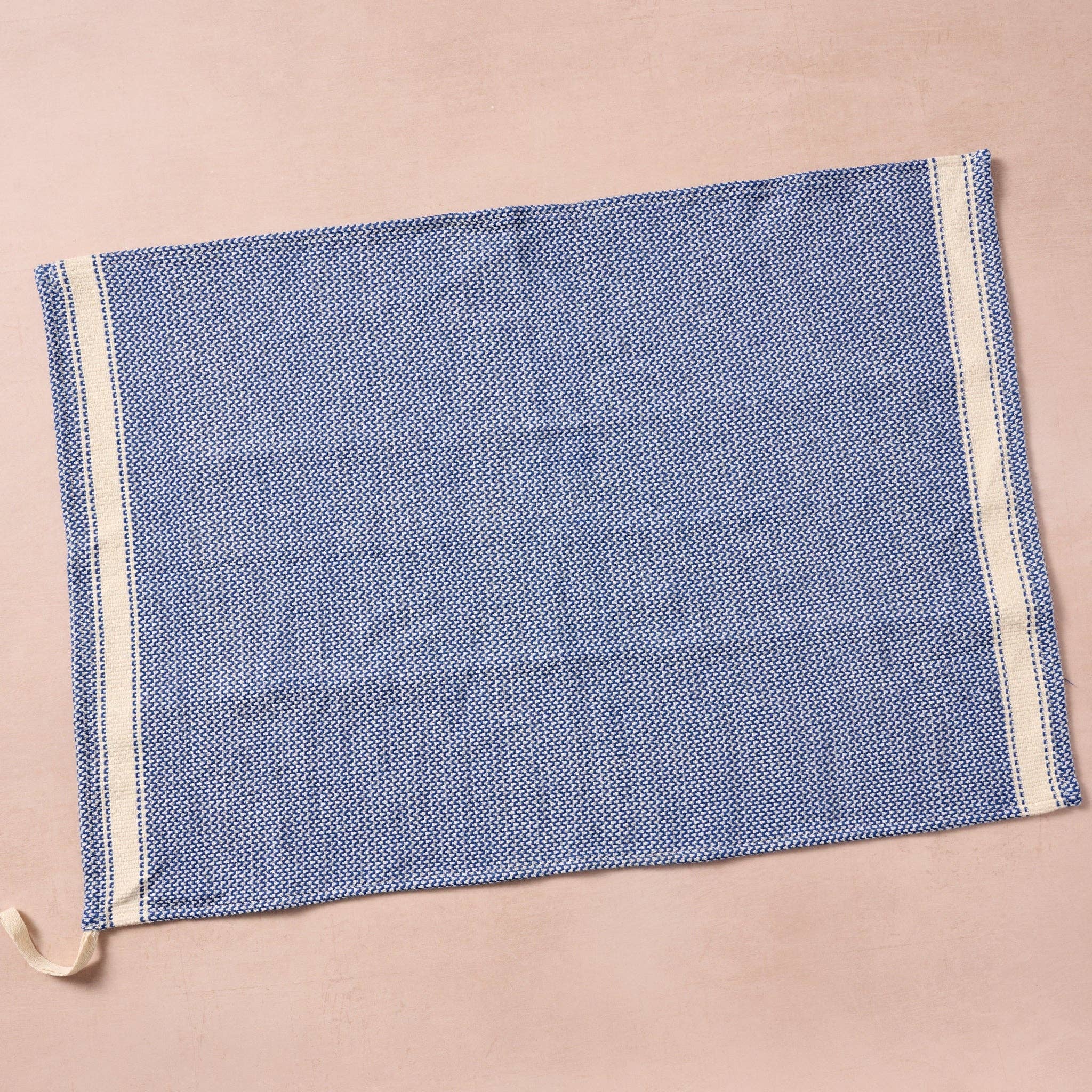 Brighten your kitchen with a pop of color and timeless charm. This striped woven tea towel blends function with simple elegance, featuring a refreshing blue and white base accented by three bold tan stripes at each end. Crafted from 100% cotton, it’s soft, absorbent and ready to tackle daily tasks - from drying dishes to lining a breadbasket. A convenient cotton loop in the corner makes it easy to hang and display. Whether you’re cooking up memories or cleaning up spills, this towel adds a cheerful, artisan