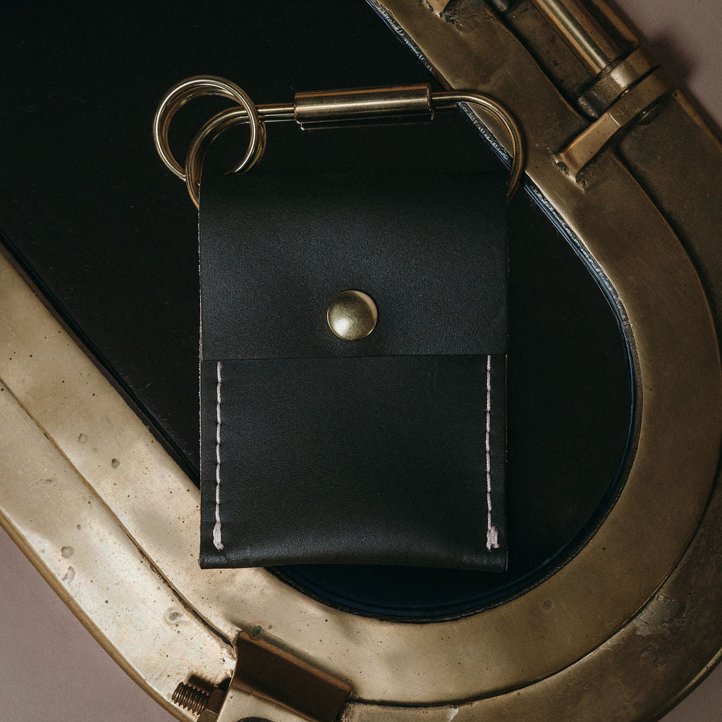 A black Nan Wallet made of leather and white stitching with a gold-colored ring. 