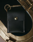 A black Nan Wallet made of leather and white stitching with a gold-colored ring. 