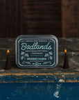 Badlands incense cones packaging with two lit incense cones on a rustic wooden surface.