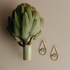 Ozona teardrop earrings with green jasper stones beside an artichoke on a tan background