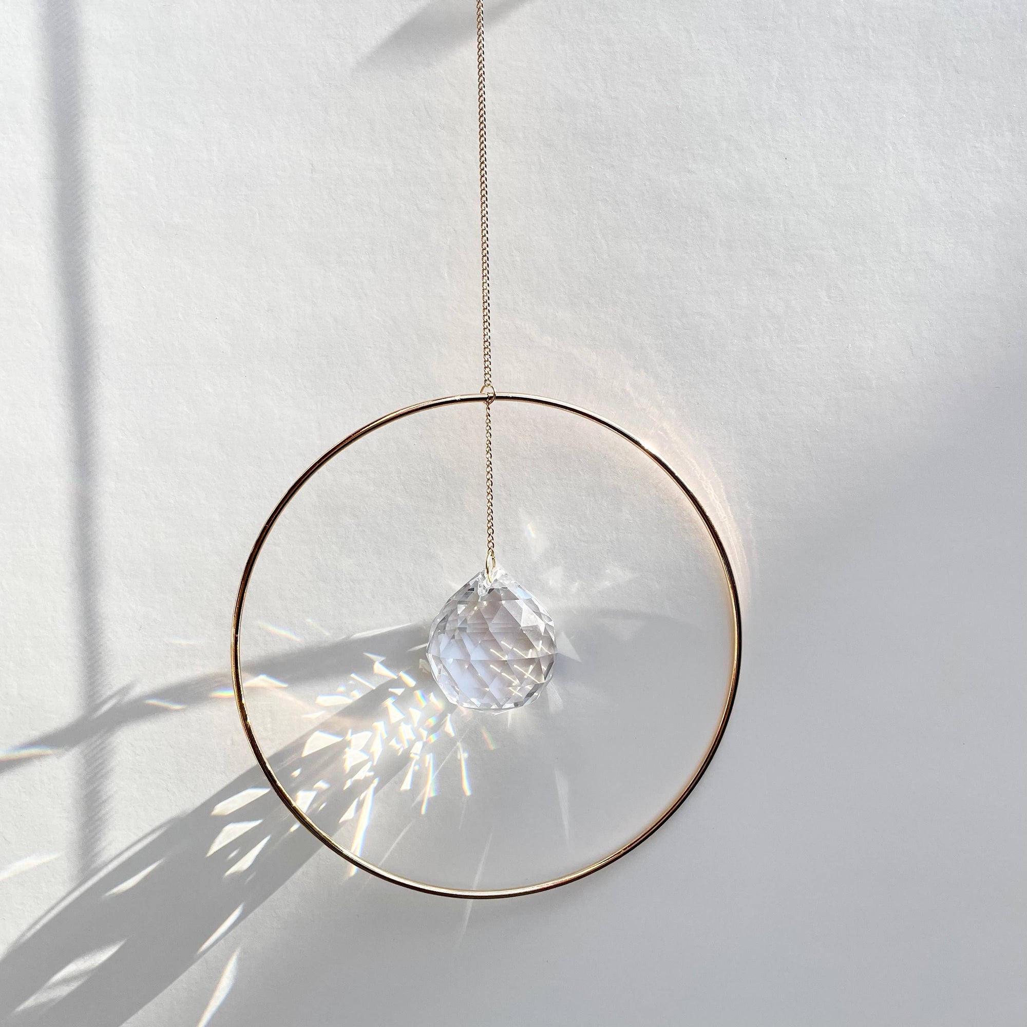 Bring a little sparkle and magic into your home with Prism Ring Suncatchers. Each piece features a golden ring with a prism suspended at its center, designed to catch sunlight and scatter tiny rainbows across your walls and floors. Hang it in a bright window or on a wall to add a touch of light-filled beauty to your space.