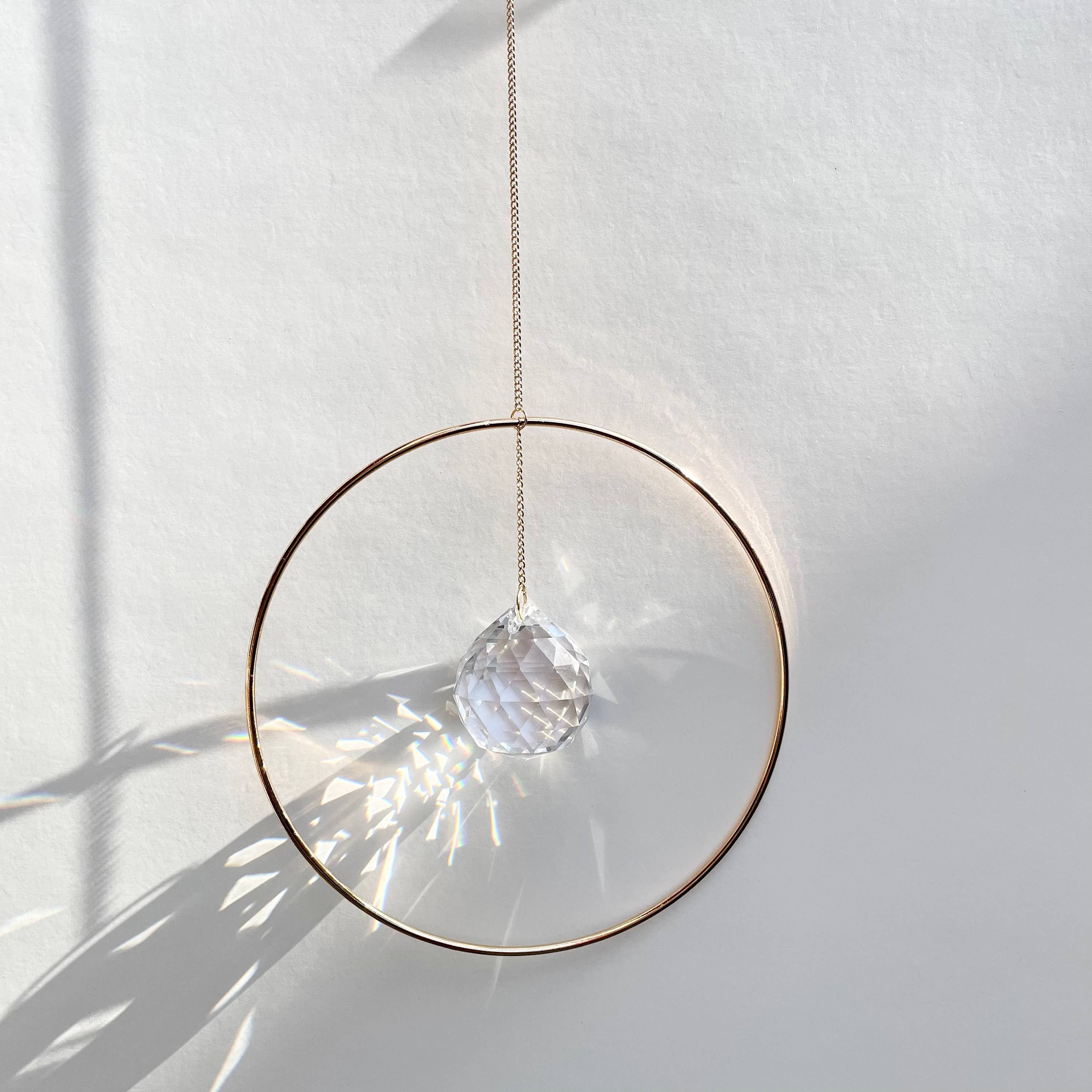 Bring a little sparkle and magic into your home with Prism Ring Suncatchers. Each piece features a golden ring with a prism suspended at its center, designed to catch sunlight and scatter tiny rainbows across your walls and floors. Hang it in a bright window or on a wall to add a touch of light-filled beauty to your space.