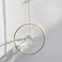 Gold ring suncatcher with a clear crystal prism hanging against a white wall