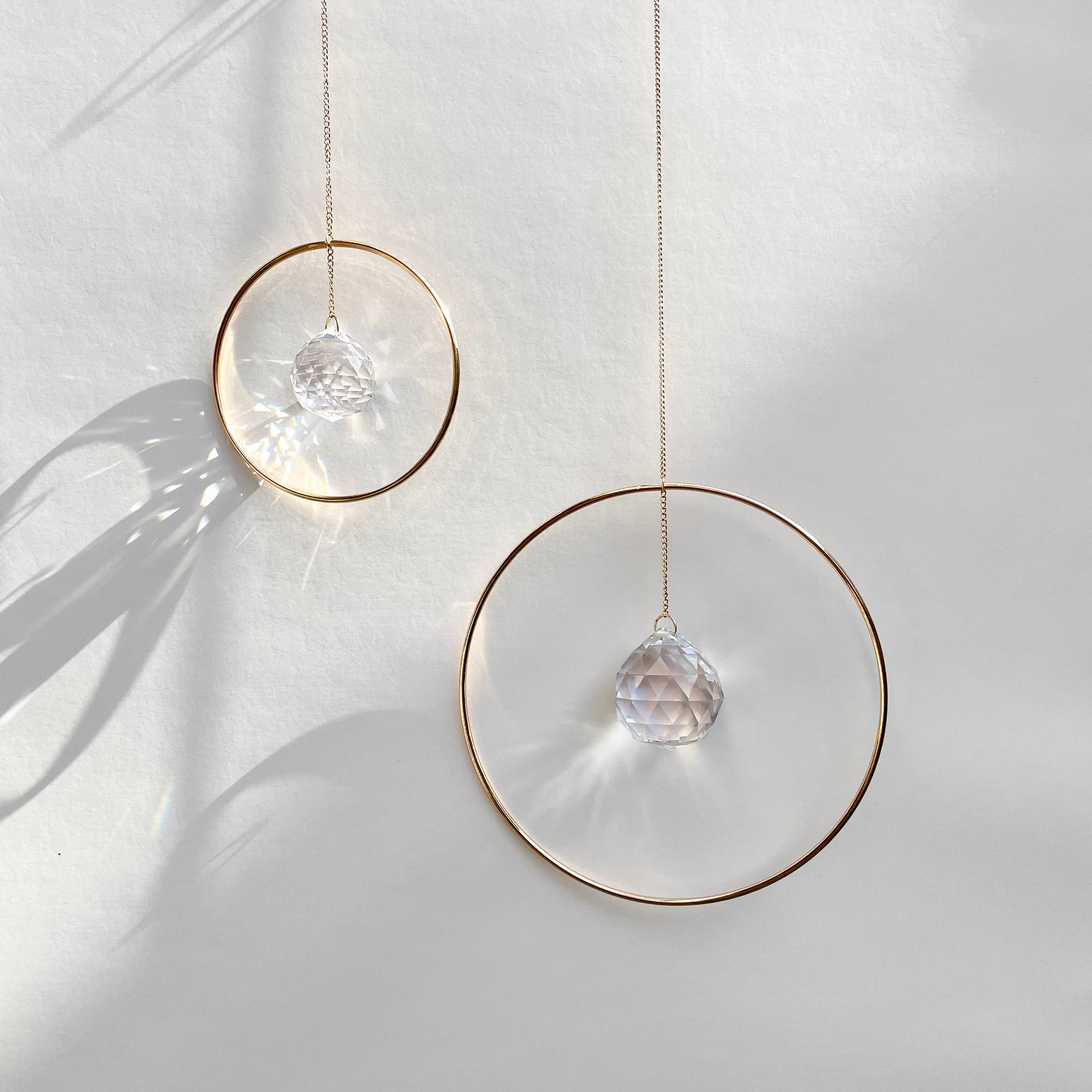 Bring a little sparkle and magic into your home with Prism Ring Suncatchers. Each piece features a golden ring with a prism suspended at its center, designed to catch sunlight and scatter tiny rainbows across your walls and floors. Hang it in a bright window or on a wall to add a touch of light-filled beauty to your space.