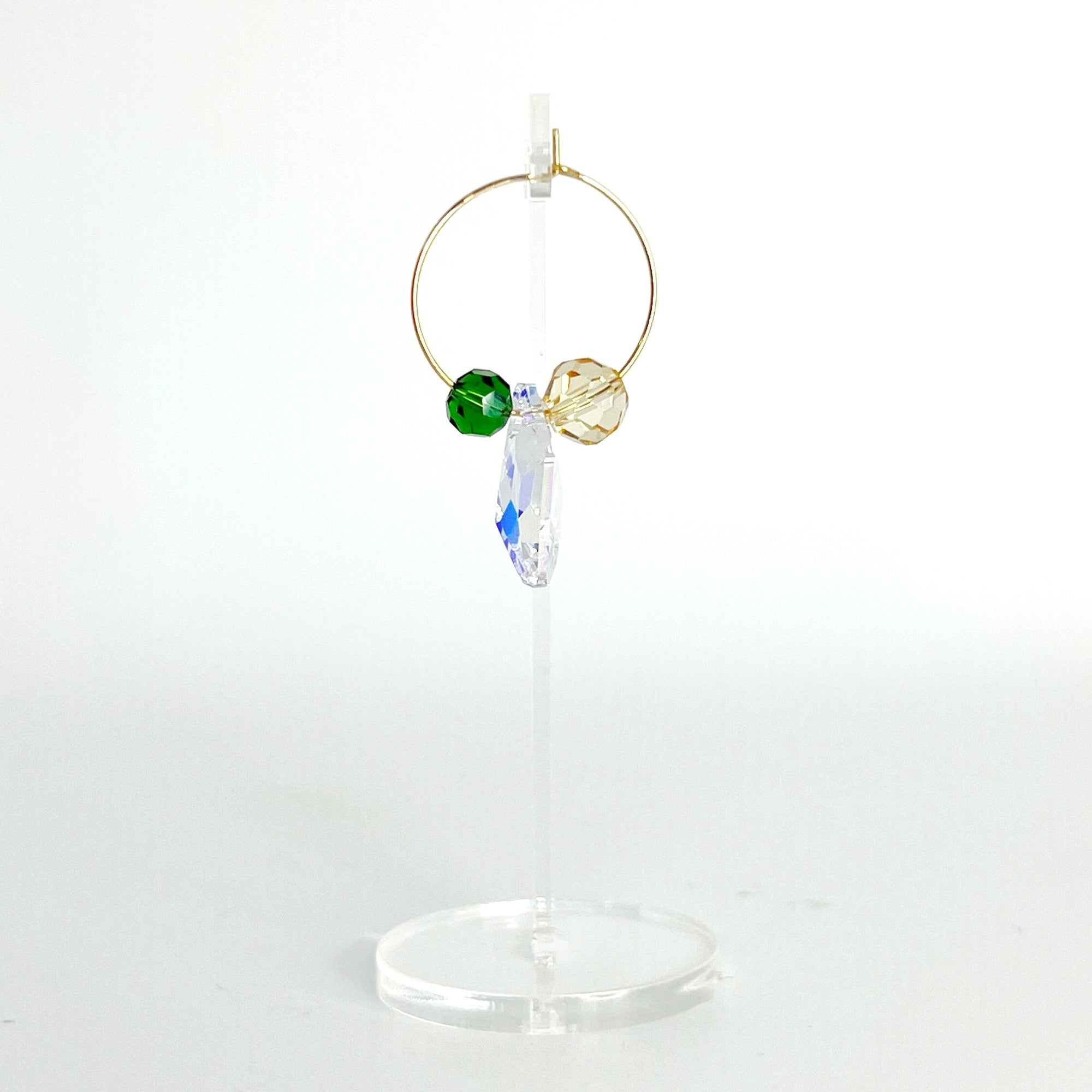 Understated elegance with a twist. The Small Muse Hoops combine a soft champagne crystal and a rich emerald green stone to frame an asymmetrical feature crystal at the center. The result is a beautifully balanced mix of refinement and individuality—perfect for the quietly powerful.