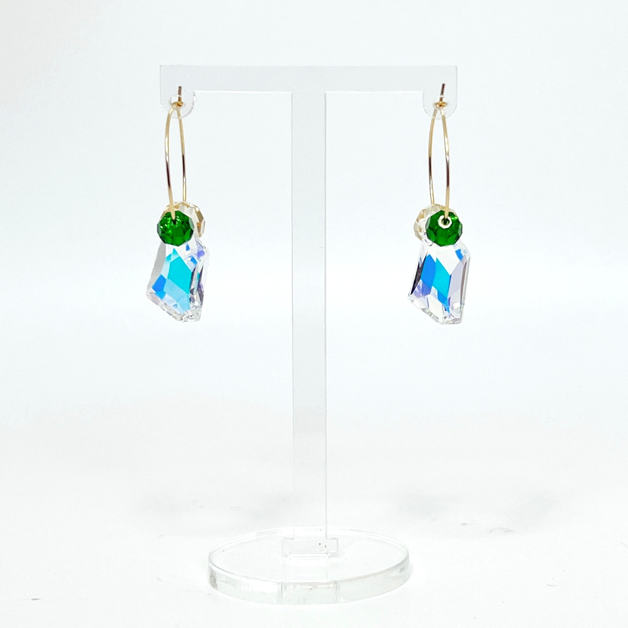 Understated elegance with a twist. The Small Muse Hoops combine a soft champagne crystal and a rich emerald green stone to frame an asymmetrical feature crystal at the center. The result is a beautifully balanced mix of refinement and individuality—perfect for the quietly powerful.