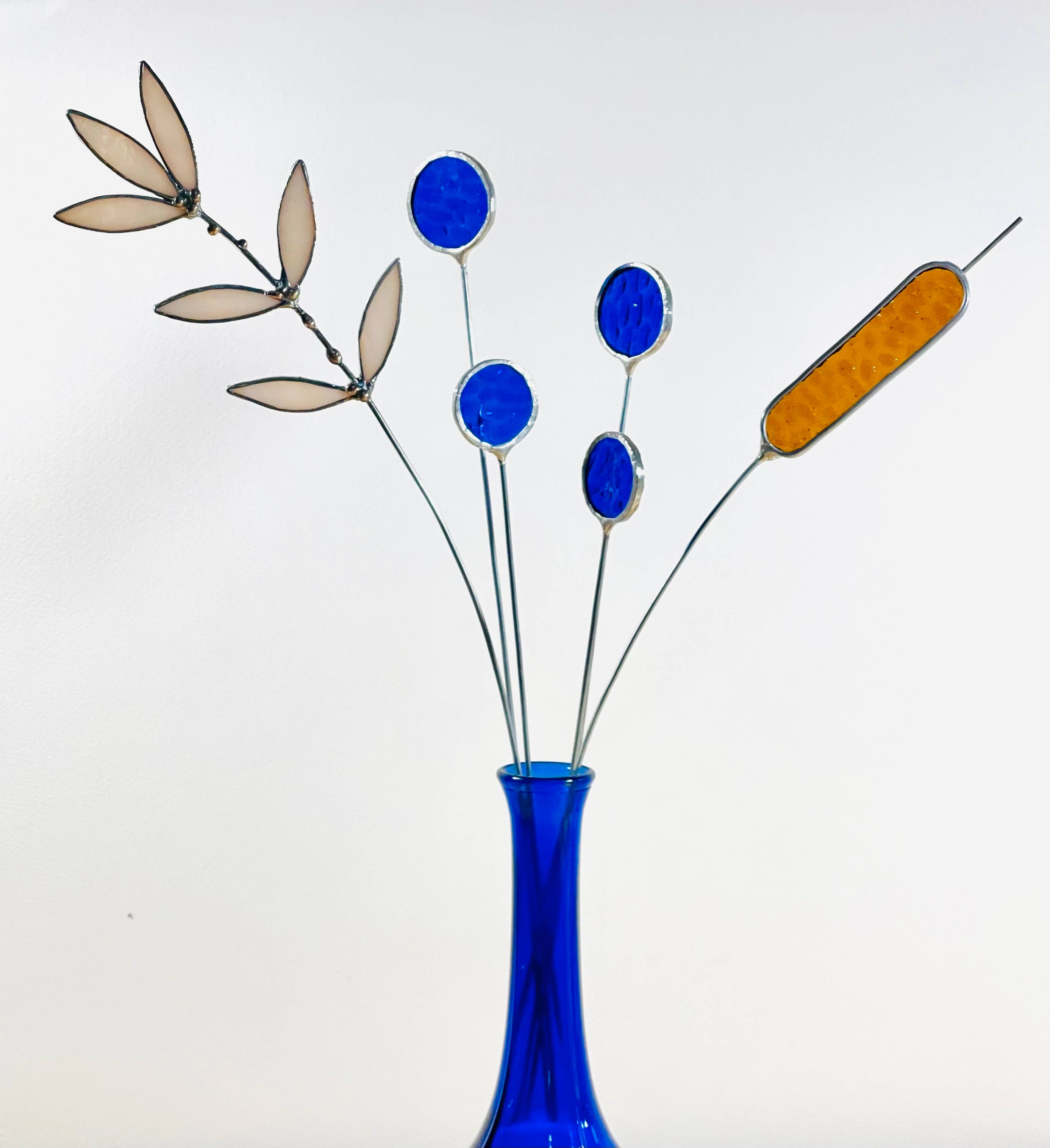 Bring a pop of color and artistry to your home with this handcrafted set of stained glass blue globe thistles by Samara Designs Studio. Each stem is carefully handmade using cobalt blue stained glass, cut and assembled with care to create a lasting botanical accent that will never wilt or fade.