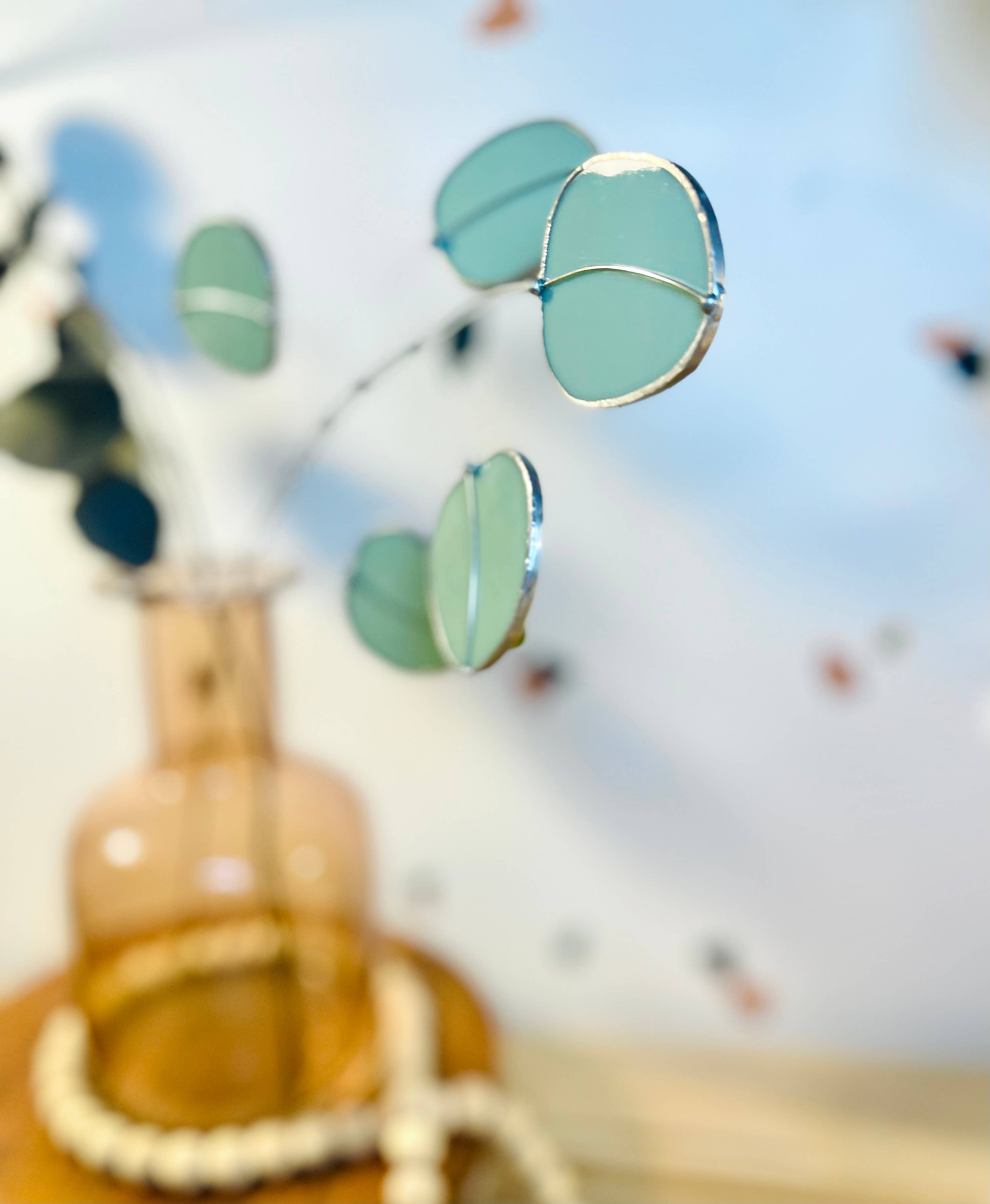 Bring a pop of color and artistry to your home with this handcrafted stained glass silver dollar eucalyptus stem by Samara Designs Studio. This stem is made from beautiful celadon green stained glass, carefully cut and assembled by hand to create a lasting botanical accent that will never wilt or fade.