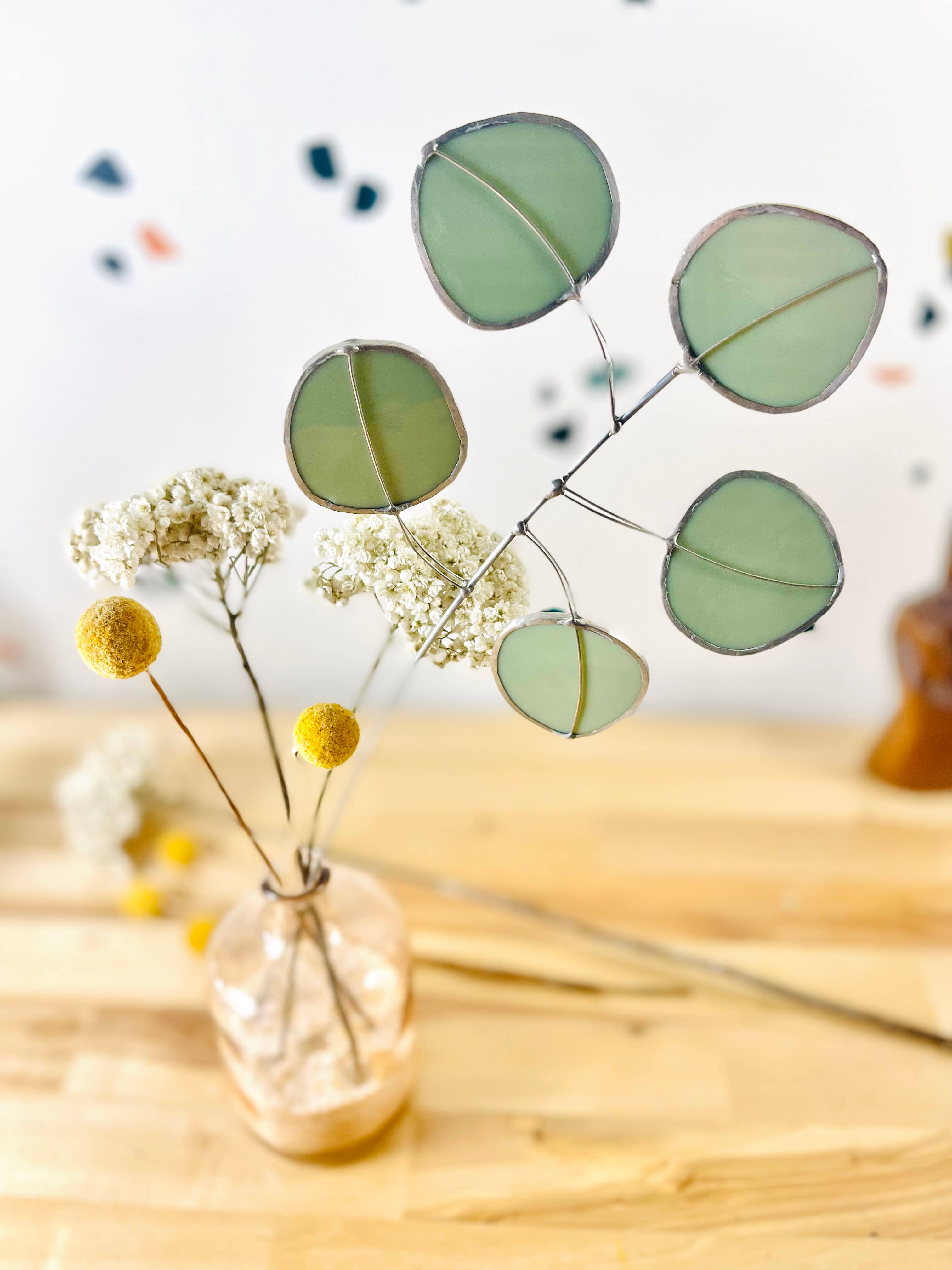 Bring a pop of color and artistry to your home with this handcrafted stained glass silver dollar eucalyptus stem by Samara Designs Studio. This stem is made from beautiful celadon green stained glass, carefully cut and assembled by hand to create a lasting botanical accent that will never wilt or fade.