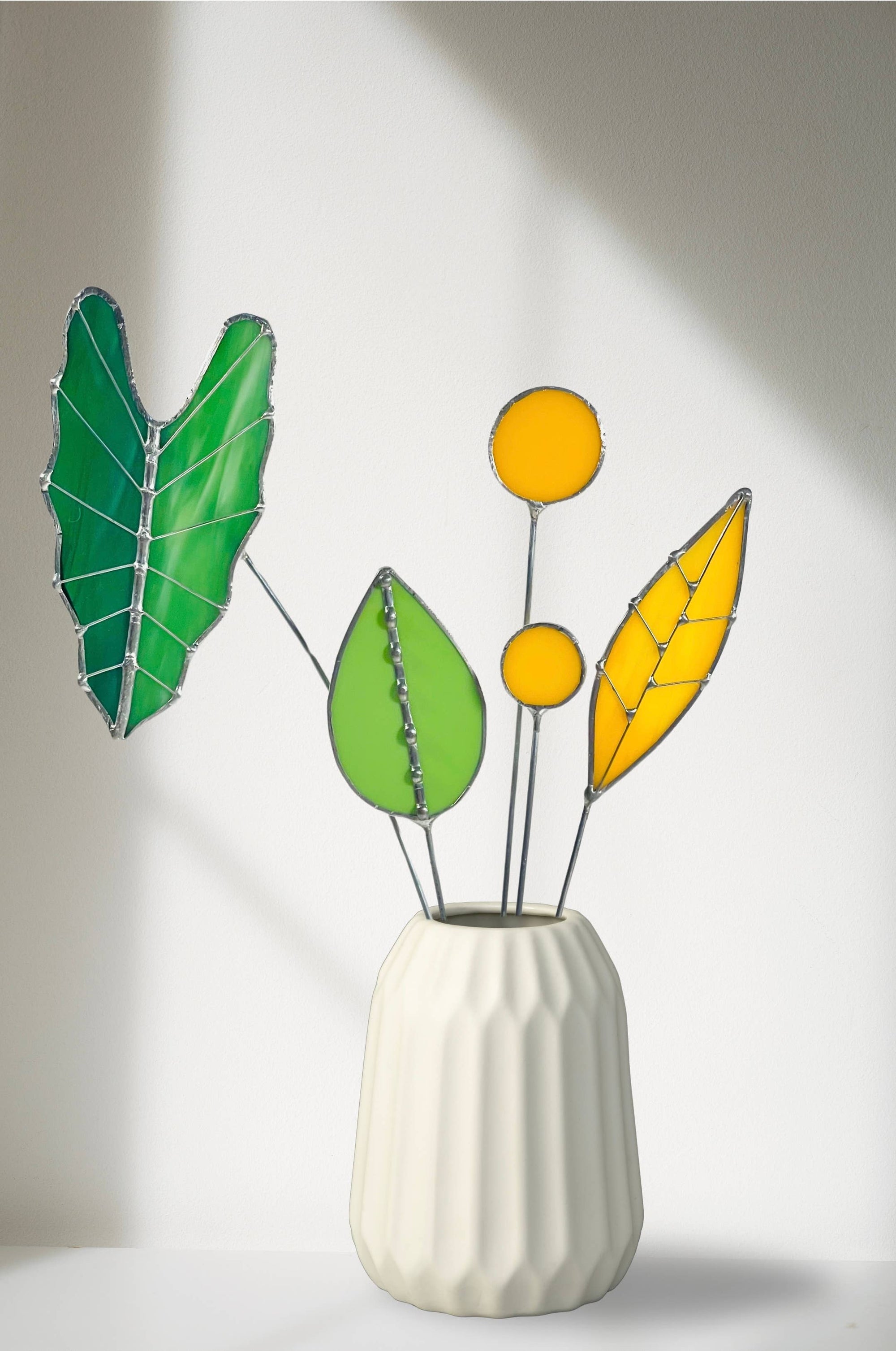 Bring a pop of color and artistry to your home with this handcrafted stained glass tropical green Alocasia leaf by Samara Designs Studio. This artistic interpretation captures the unique shape of the Alocasia leaf in lasting stained glass that will never wilt or fade. Each leaf is carefully handmade using stained glass and galvanized steel wire for a durable botanical accent.