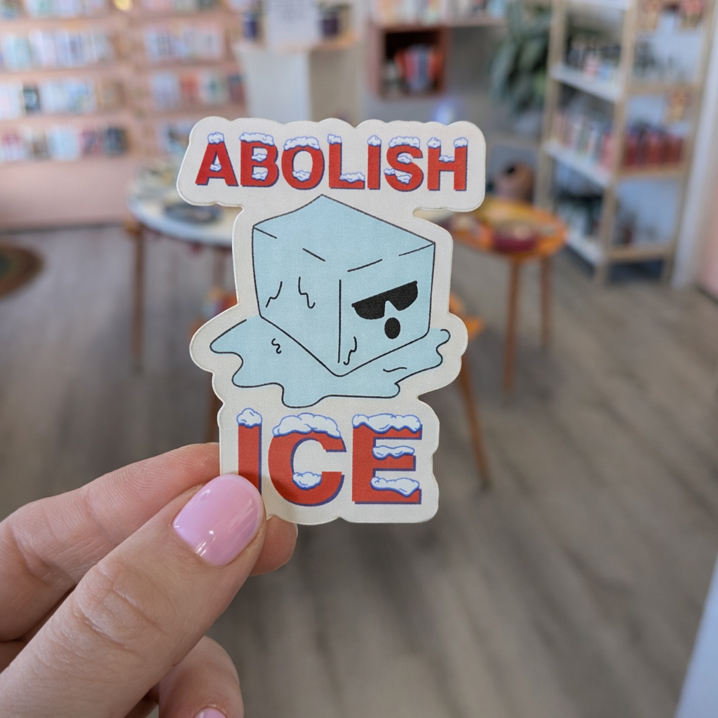 Sticker with 'ABOLISH ICE' text held in a hand against a blurred library background