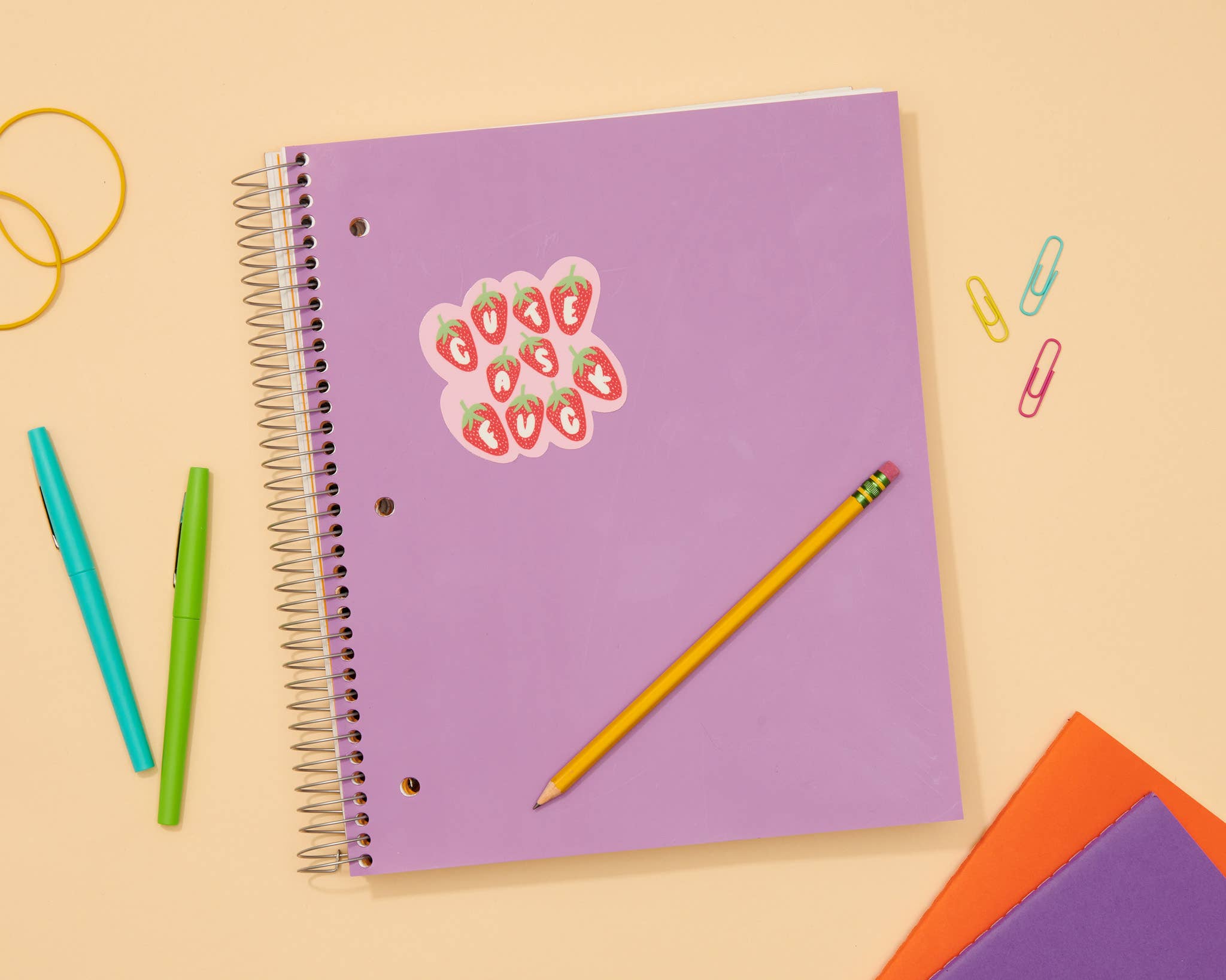 Purple spiral-bound notebook with a decorative sticker on a beige background with stationery items.