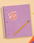 Purple spiral-bound notebook with a decorative sticker on a beige background with stationery items.