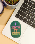 Laptop with a sticker saying 'I Hate It Here' on a desk with a candle and plant.