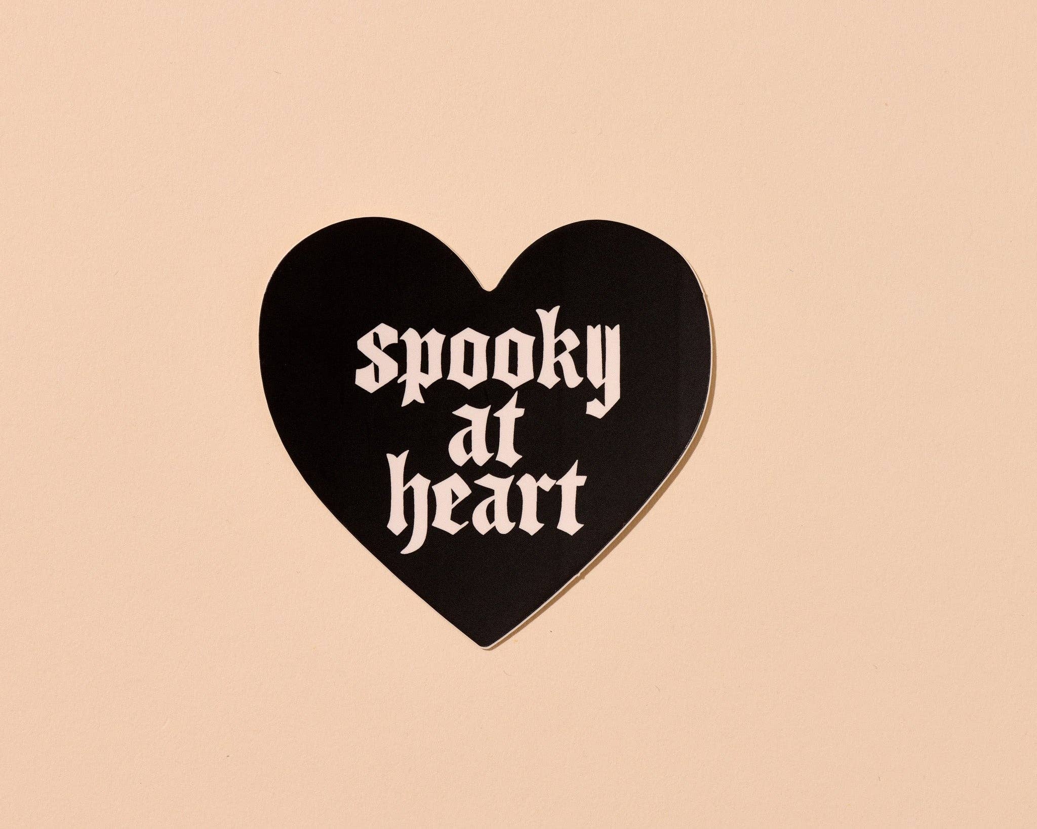 Black heart-shaped sign with 'spooky at heart' text on a beige background