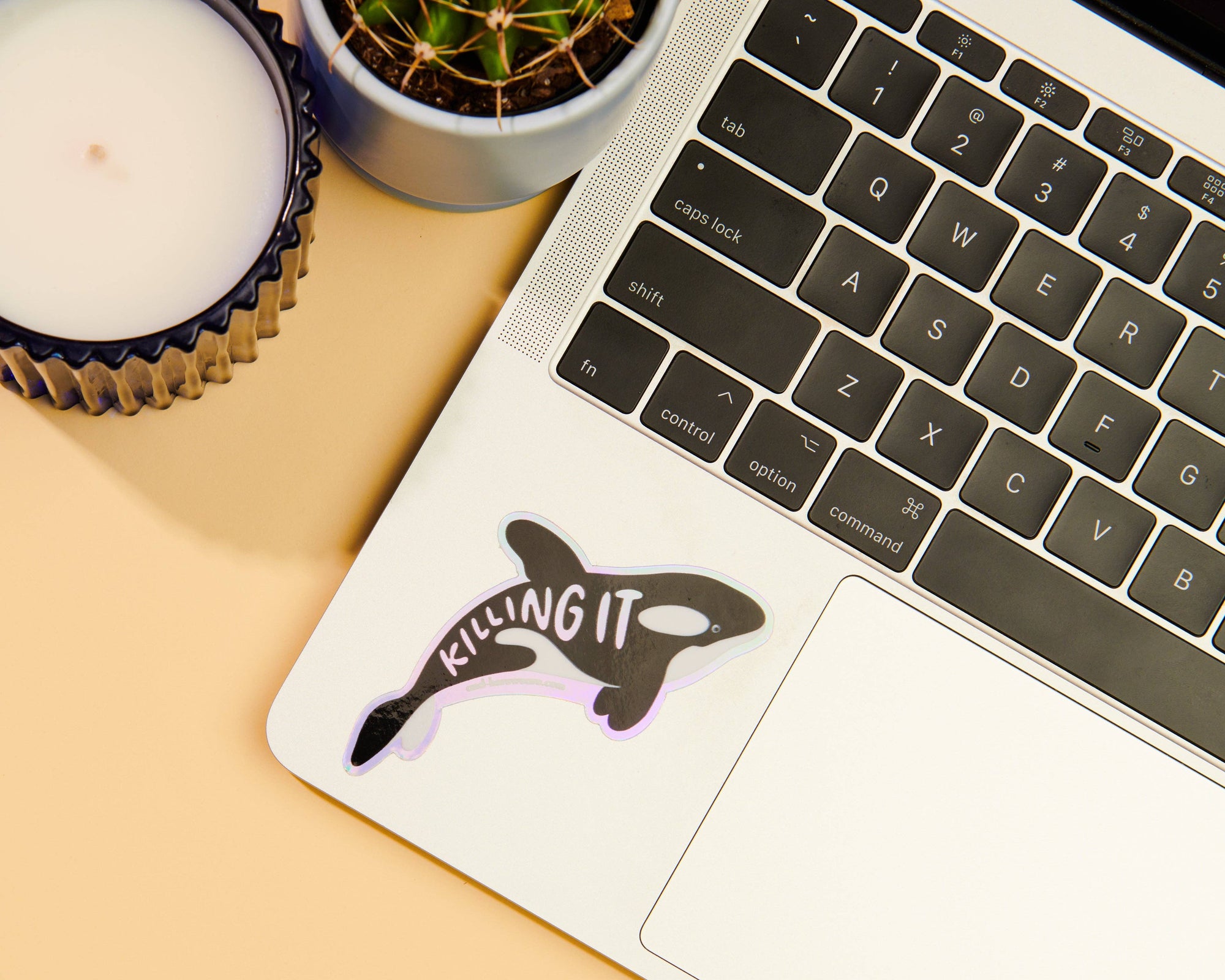 Laptop with a sticker of an orca whale and the text 'KILLING IT' on a beige surface.