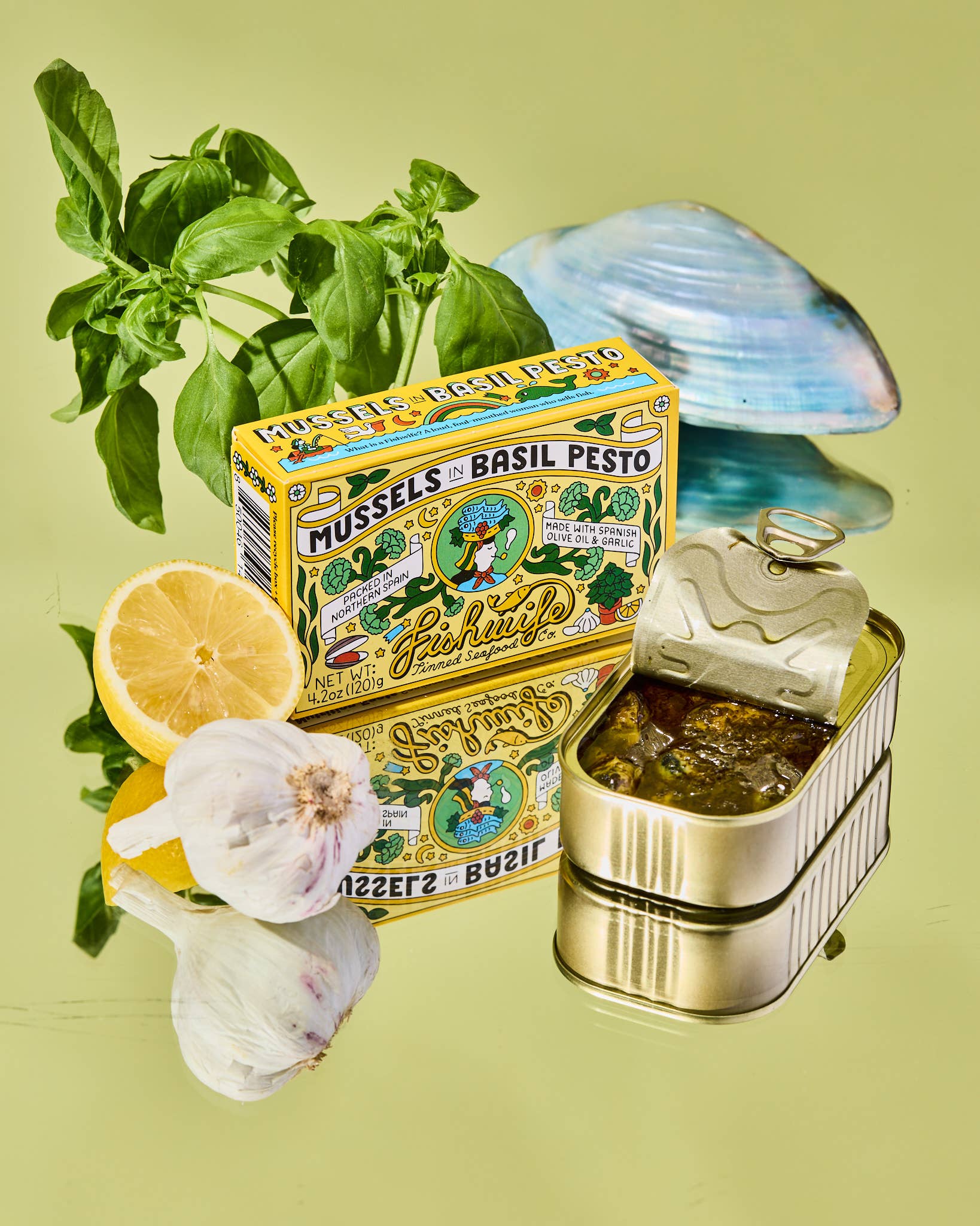Fisheduo Mussels Basil Pesto packaging with basil, lemon, and garlic on a green background