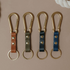 Four brass carabiner keychains with tan, olive, indigo and black leather straps