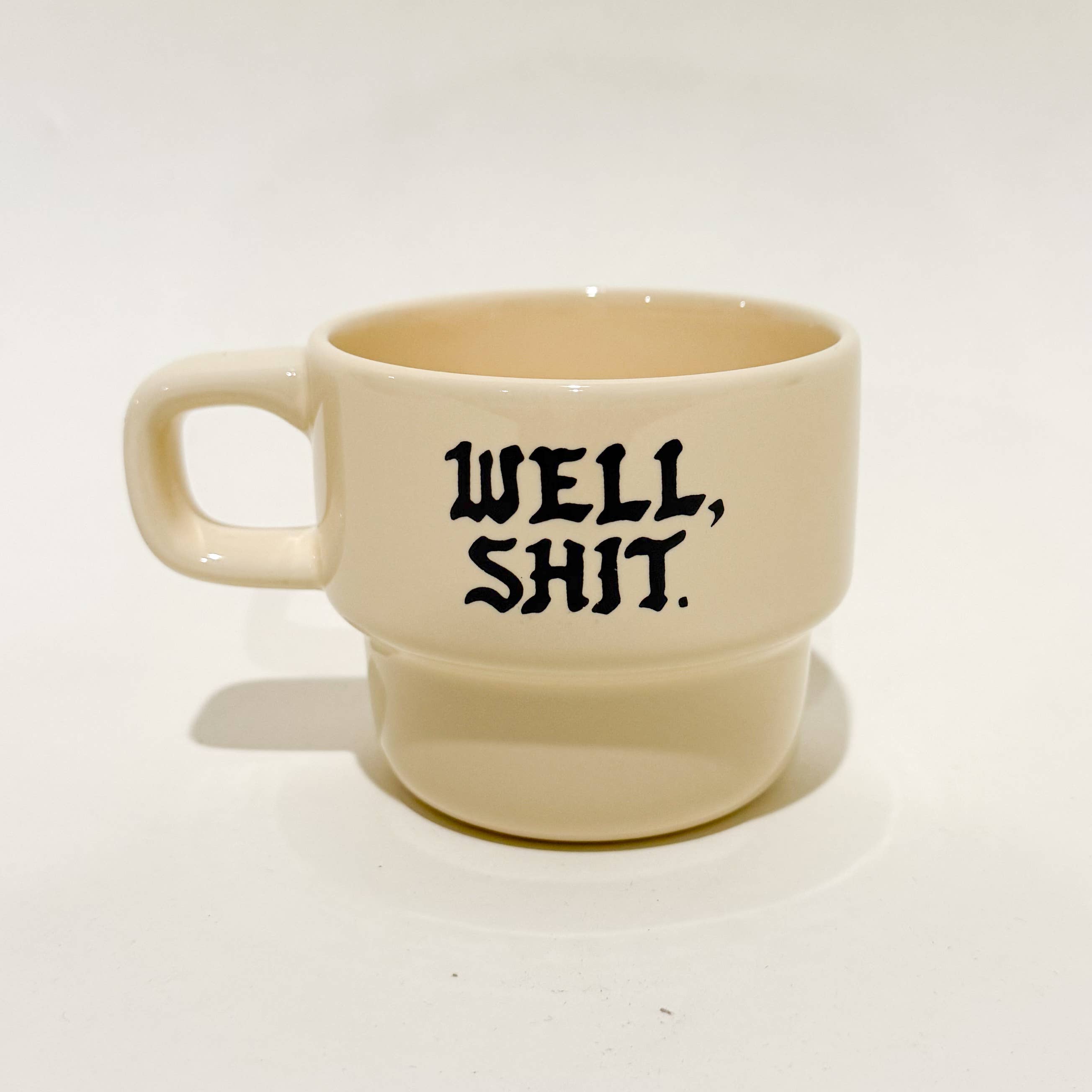 Beige mug with 'WELL, SHIT.' text on a white background