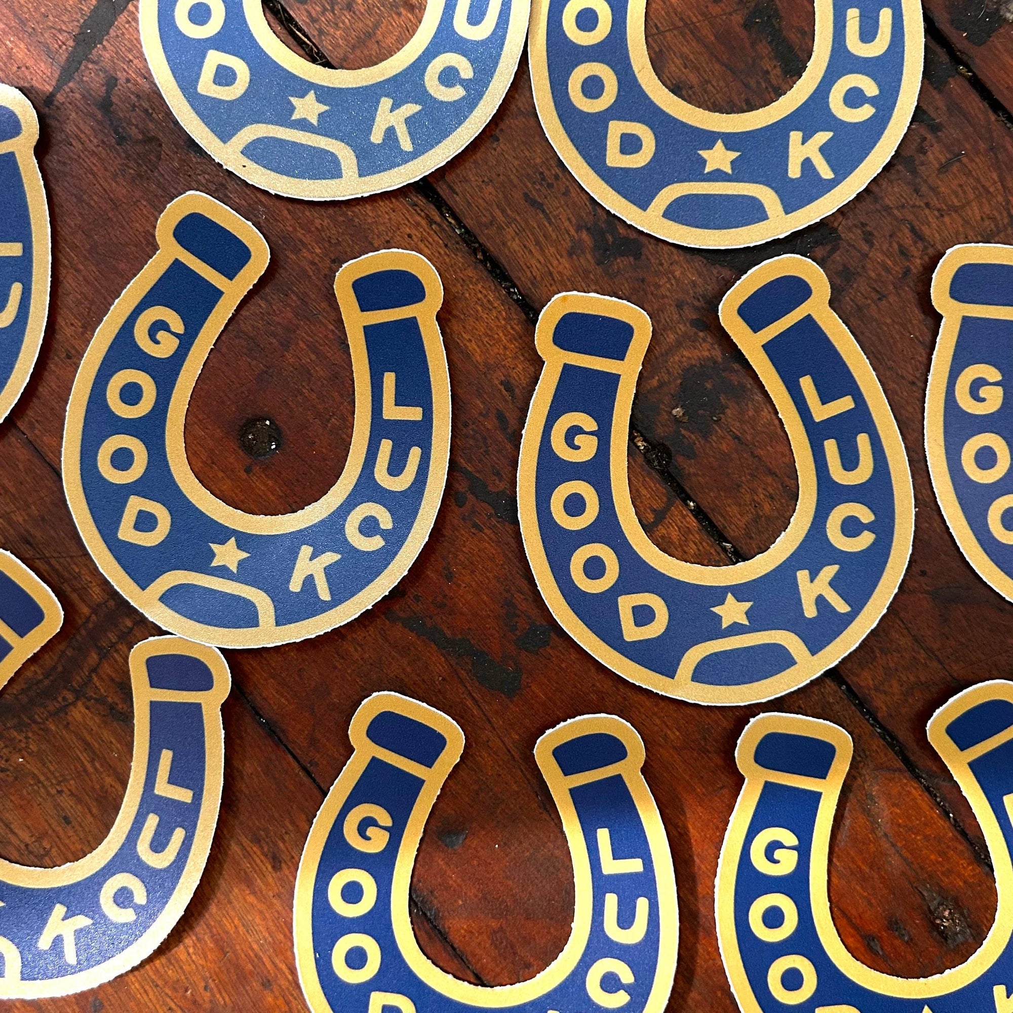 Blue and gold 'Good Luck' horseshoe stickers on a wooden surface