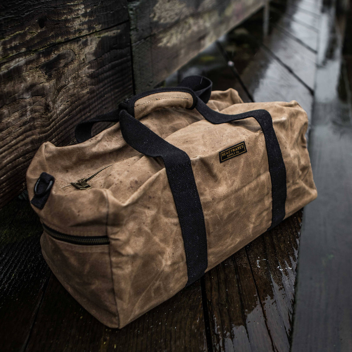 Waxed canvas duffel bag with webbing straps, padded handle and brass zipper
