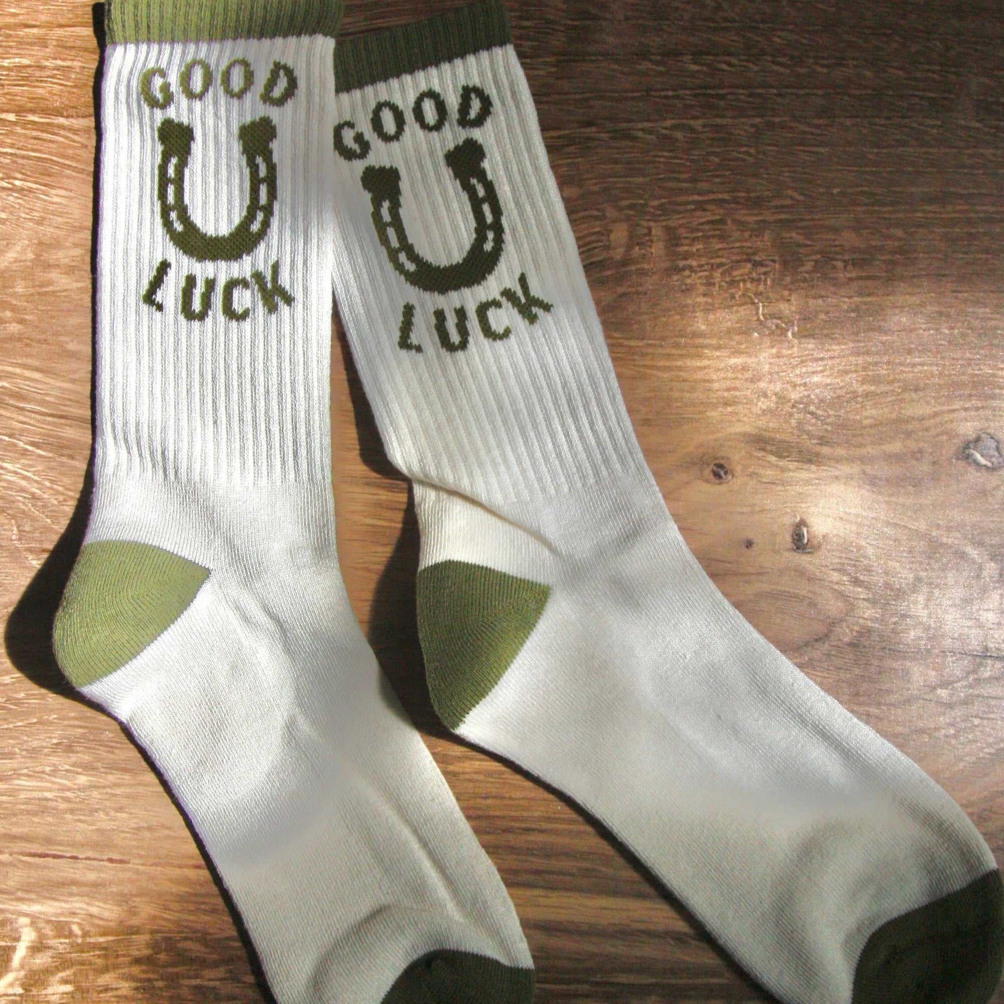 White socks with green accents and 'Good Luck' text on a wooden surface