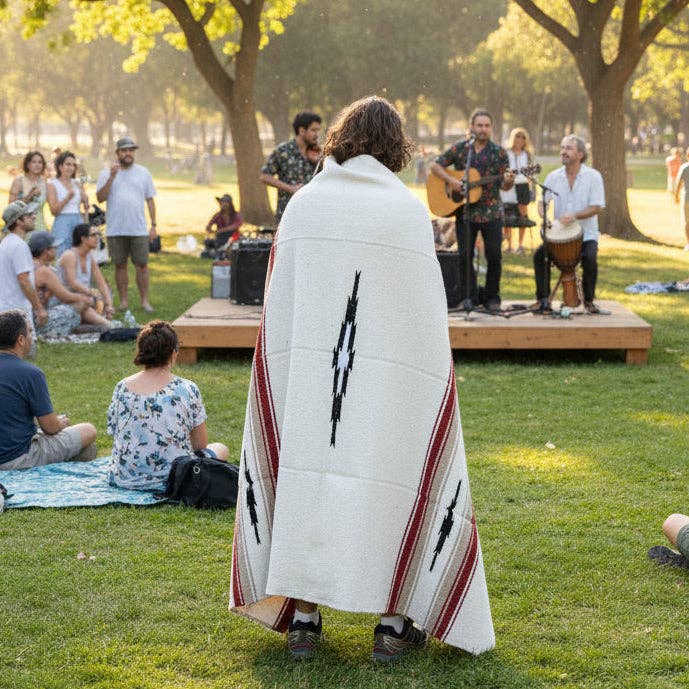 Person wrapped in a cream Desert Mesa blanket watching a band play in a park