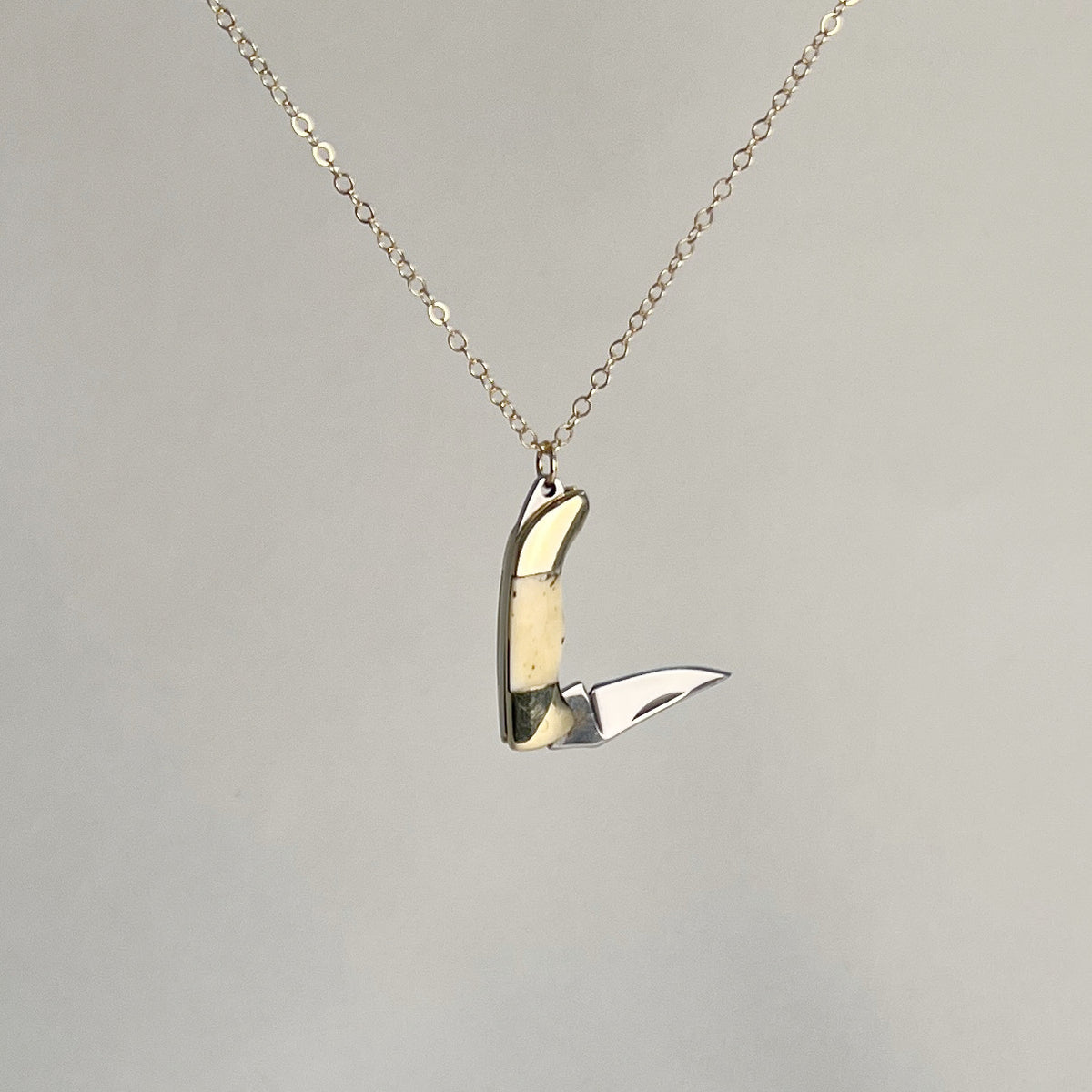 Mini bone-handled pocket knife pendant with the blade open, hanging from a gold-filled chain