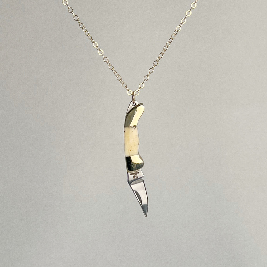 Mini bone-handled pocket knife pendant with the blade pointing down, on a gold-filled chain