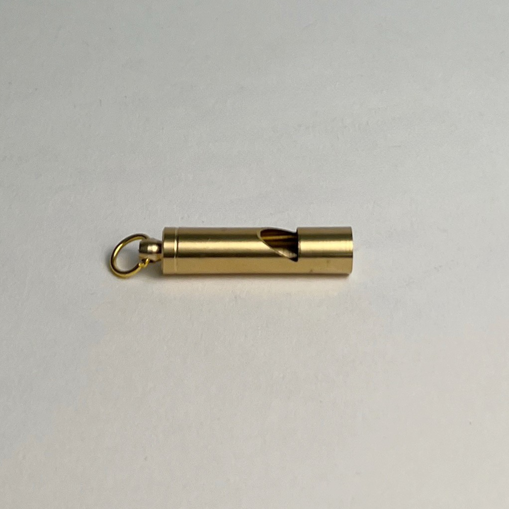 Brass whistle keychain lying on its side on a light gray background