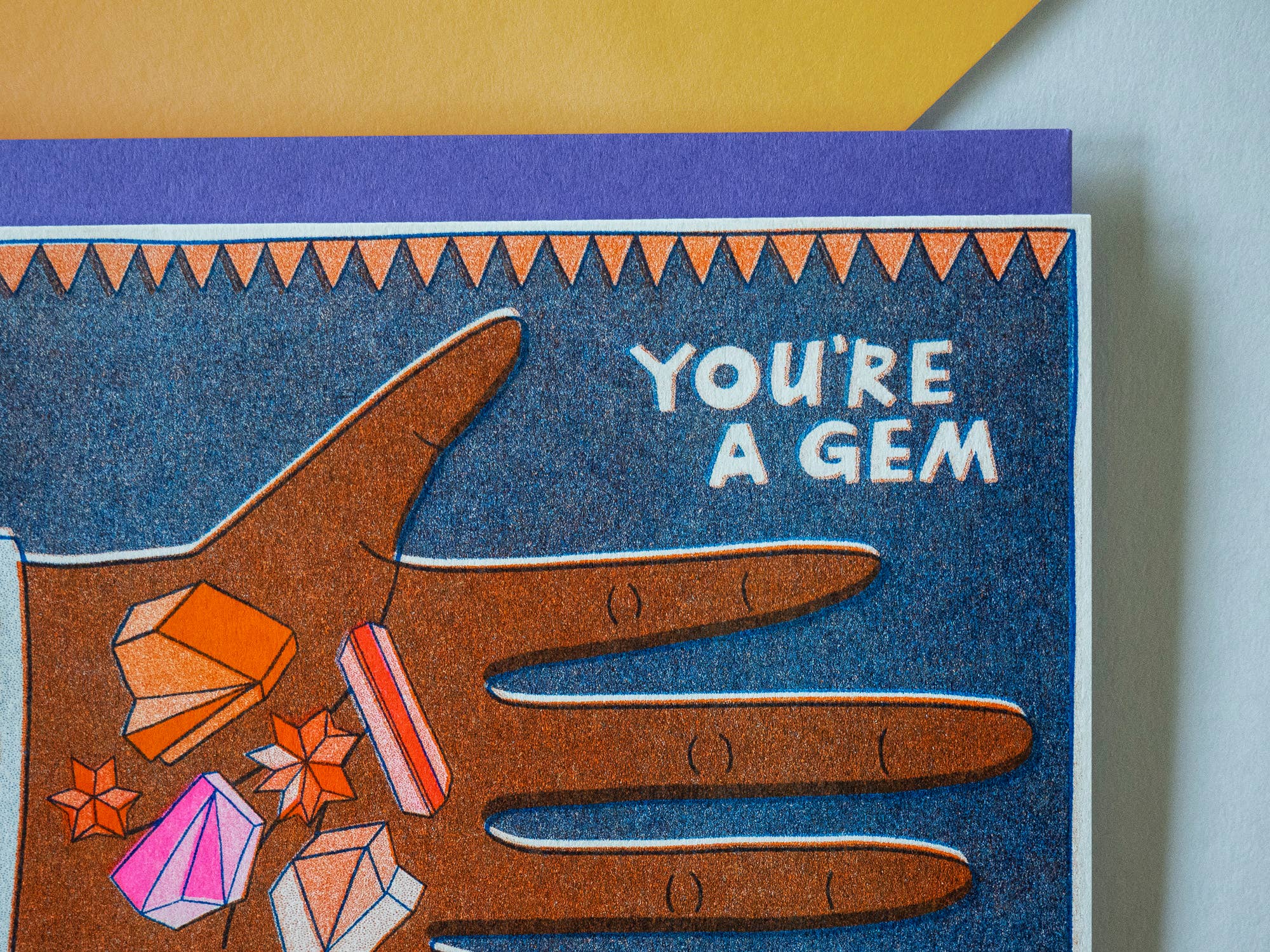 Greeting card with a hand holding gemstones and text 'You're a Gem' on a blue background.