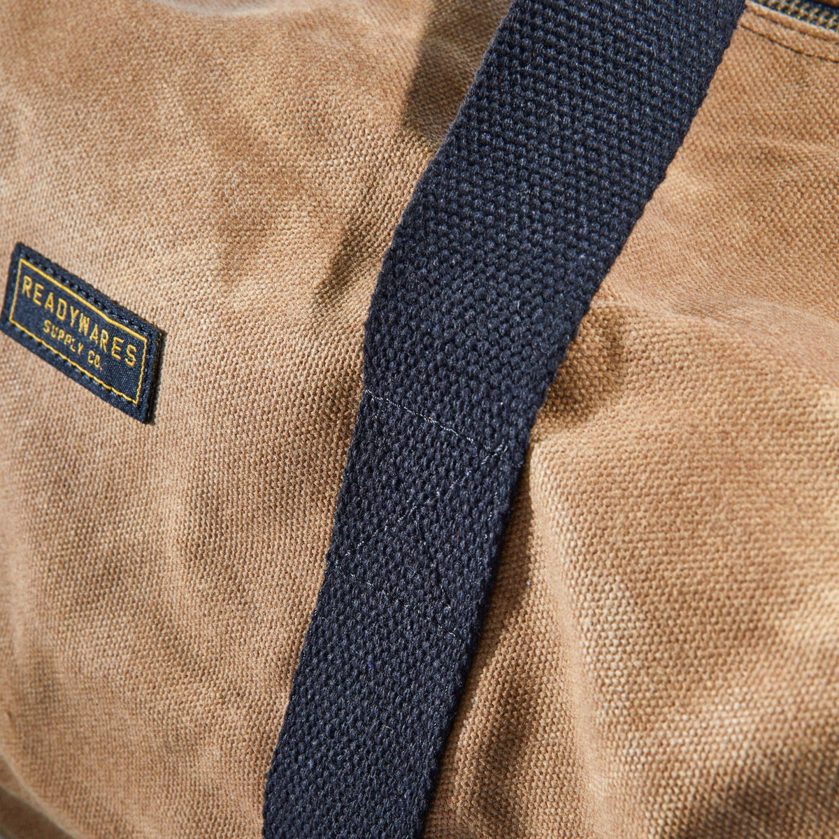 Waxed canvas duffel bag with webbing straps, padded handle and brass zipper