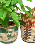 Woven basket with a green deer pattern holding a leafy plant, beside two rust and cream patterned baskets