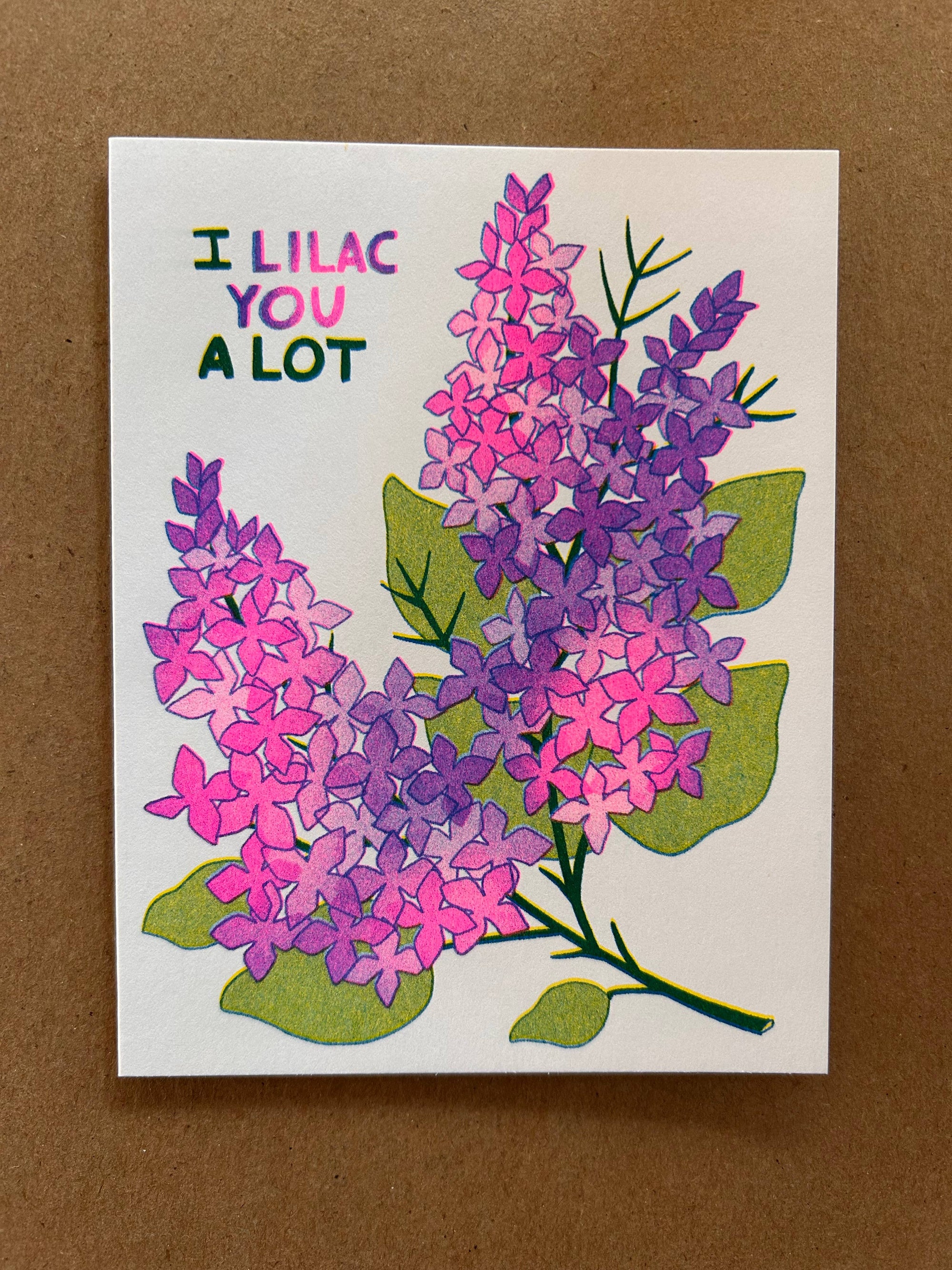 Card with pink and purple lilac flowers and text 'I Lilac You A Lot' on a brown background