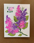 Card with pink and purple lilac flowers and text 'I Lilac You A Lot' on a brown background