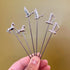 Hand holding silver cocktail picks topped with horses, geese and swords on an olive background