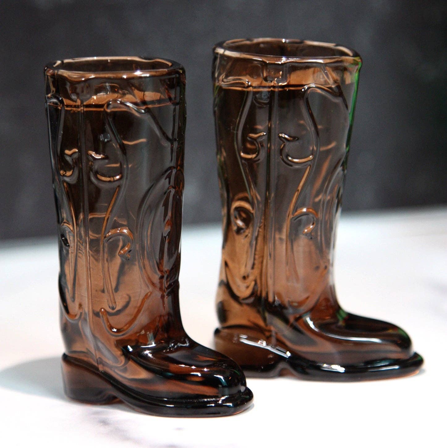 Pair of brown glass cowboy boot shot glasses on a white surface with a dark background