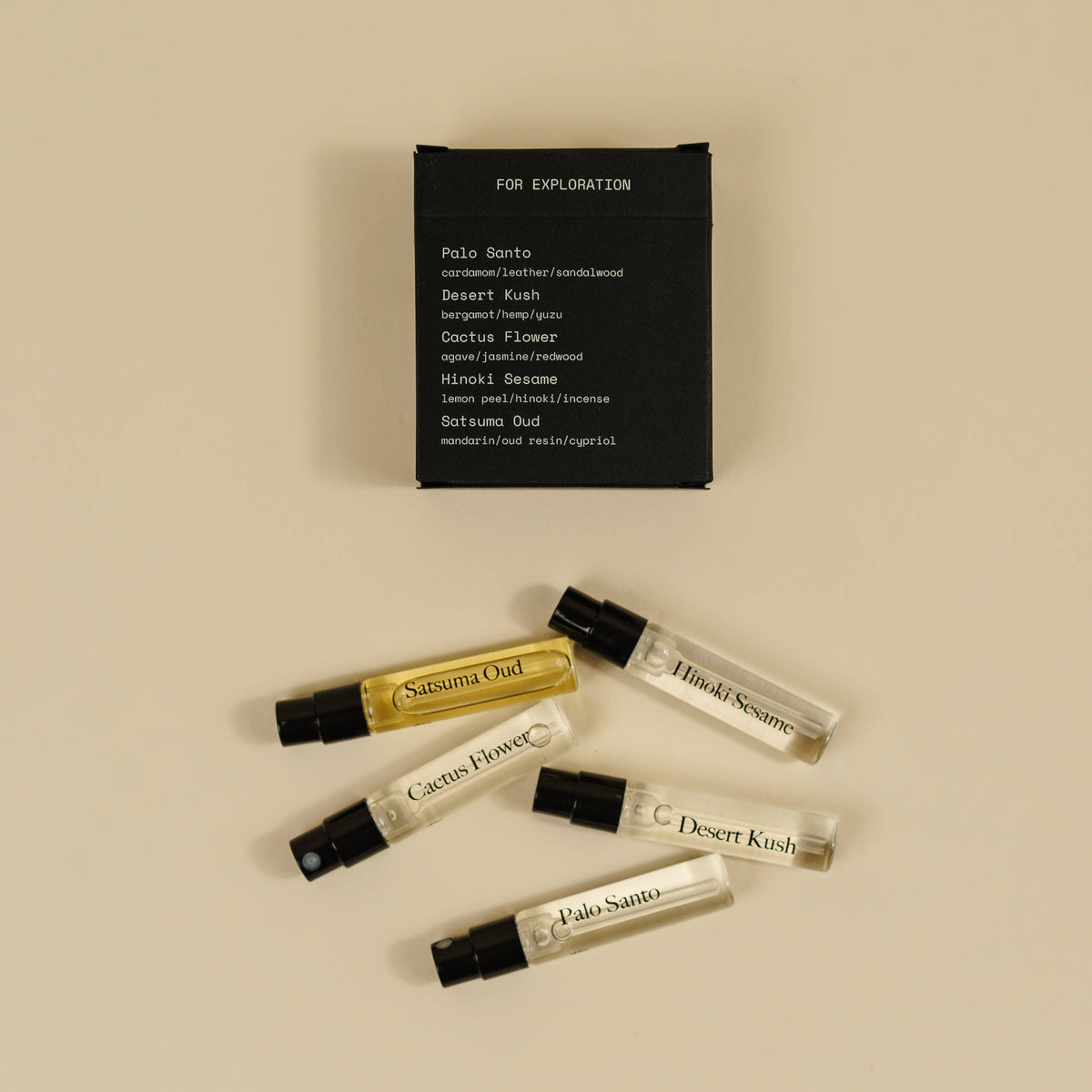 Five small perfume sample vials with black spray caps are arranged on a warm beige background below a black rectangular card labeled 'FOR EXPLORATION' and 'Pola Santo.' The vials contain clear and golden liquids, and several are labeled with scent names such as 'Sakura Odor,' 'Hawaii Scent,' 'Cactus Flower,' 'Desert Kosh,' and 'Pola Santo.