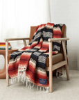 Navy, black, cream and red striped falsa blanket with a diamond band draped over a wooden armchair
