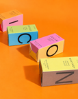 Icons perfume boxes for Dolly, Betsey, Julia and Whitney laid out to spell ICON on an orange background