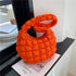 Orange quilted puffy shoulder bag on a black shelf