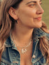 Smiling woman in a denim jacket wearing an arc earring and layered necklaces outdoors