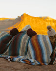 Three people wrapped in striped blankets sitting in the desert at sunset