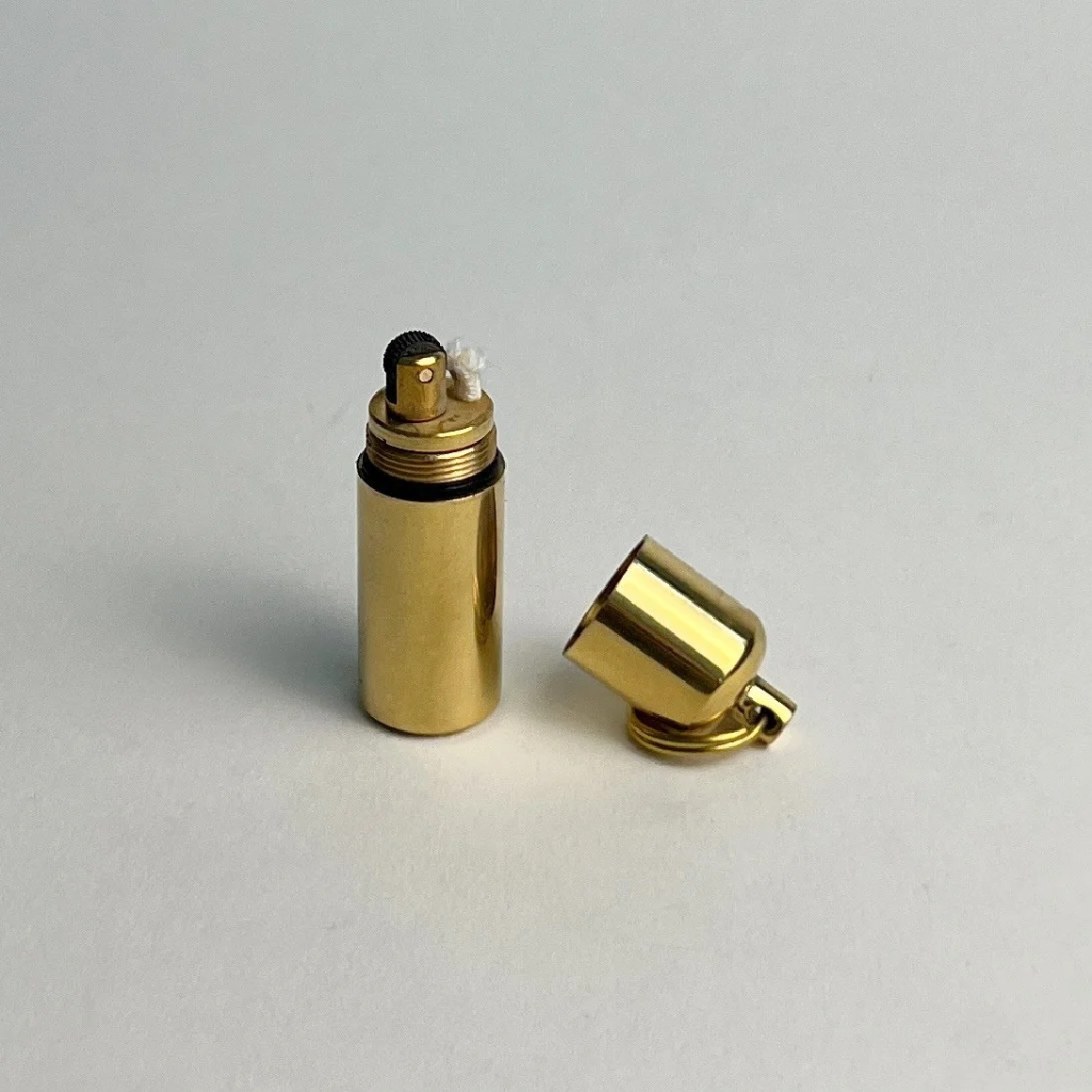 Brass capsule keychain lighter with its cap unscrewed on a gray background