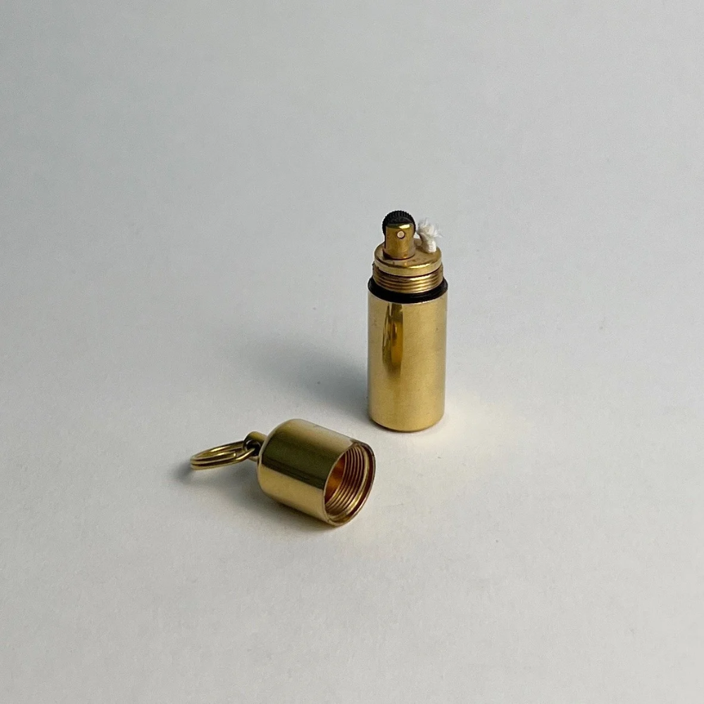 Brass keychain lighter open, with the cap and key ring lying beside it