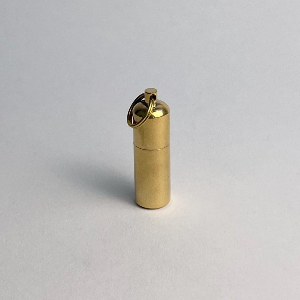 Closed brass capsule keychain lighter standing upright on a gray background