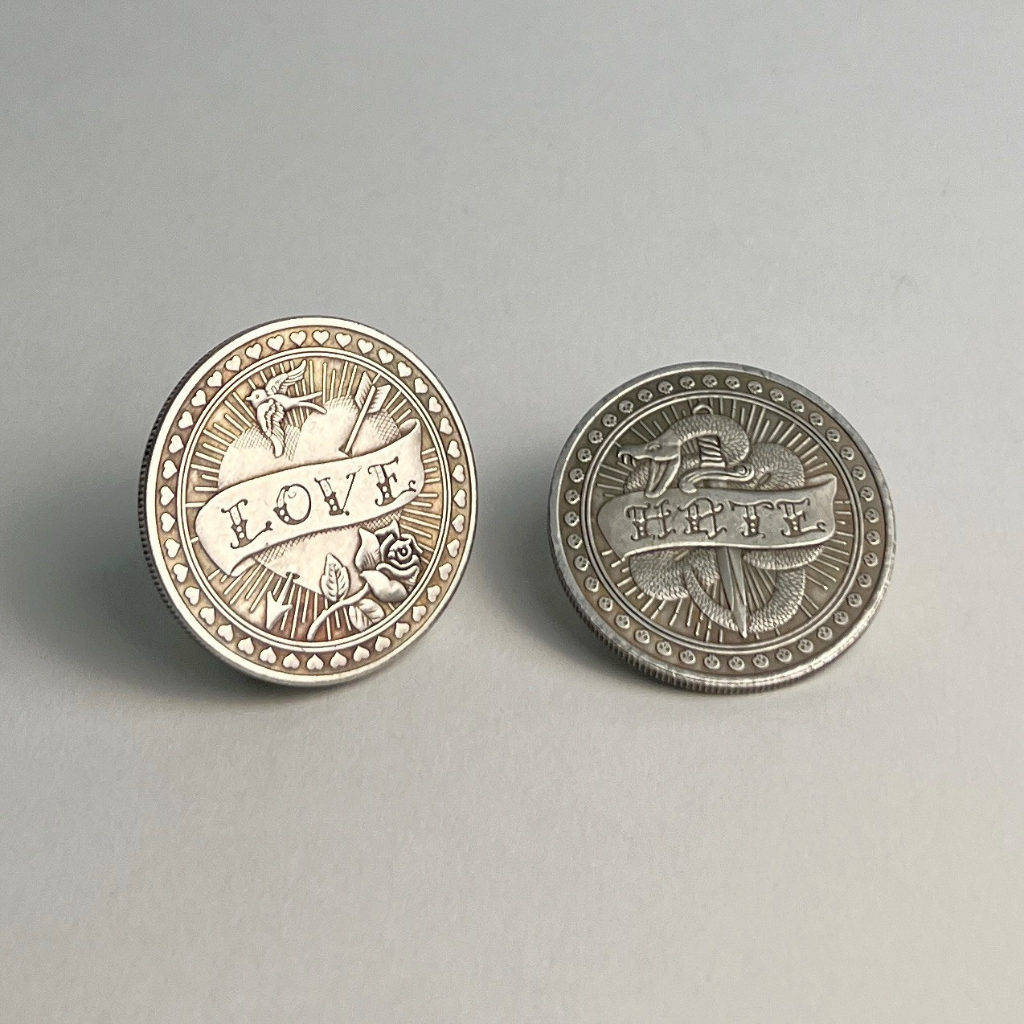 Two silver-toned flip coins, one showing LOVE and one showing HATE, on a light gray background
