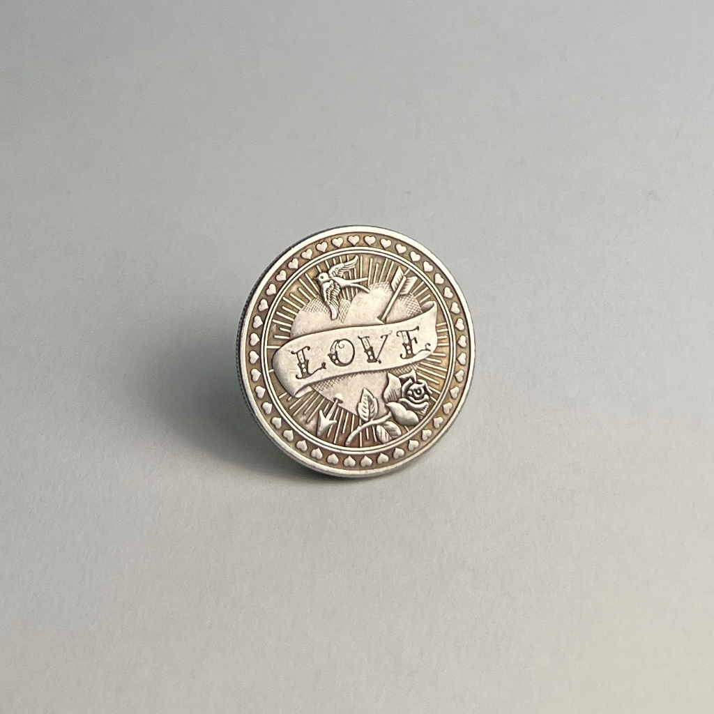 Silver-toned coin with LOVE on a banner, standing on a light gray background
