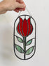 Hand holding an oval stained glass suncatcher with a red tulip